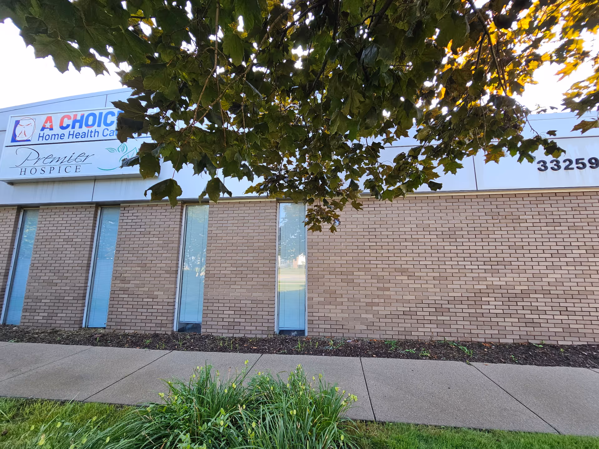 Exterior brick wall and signage of A Choice Home Health Care building with trees