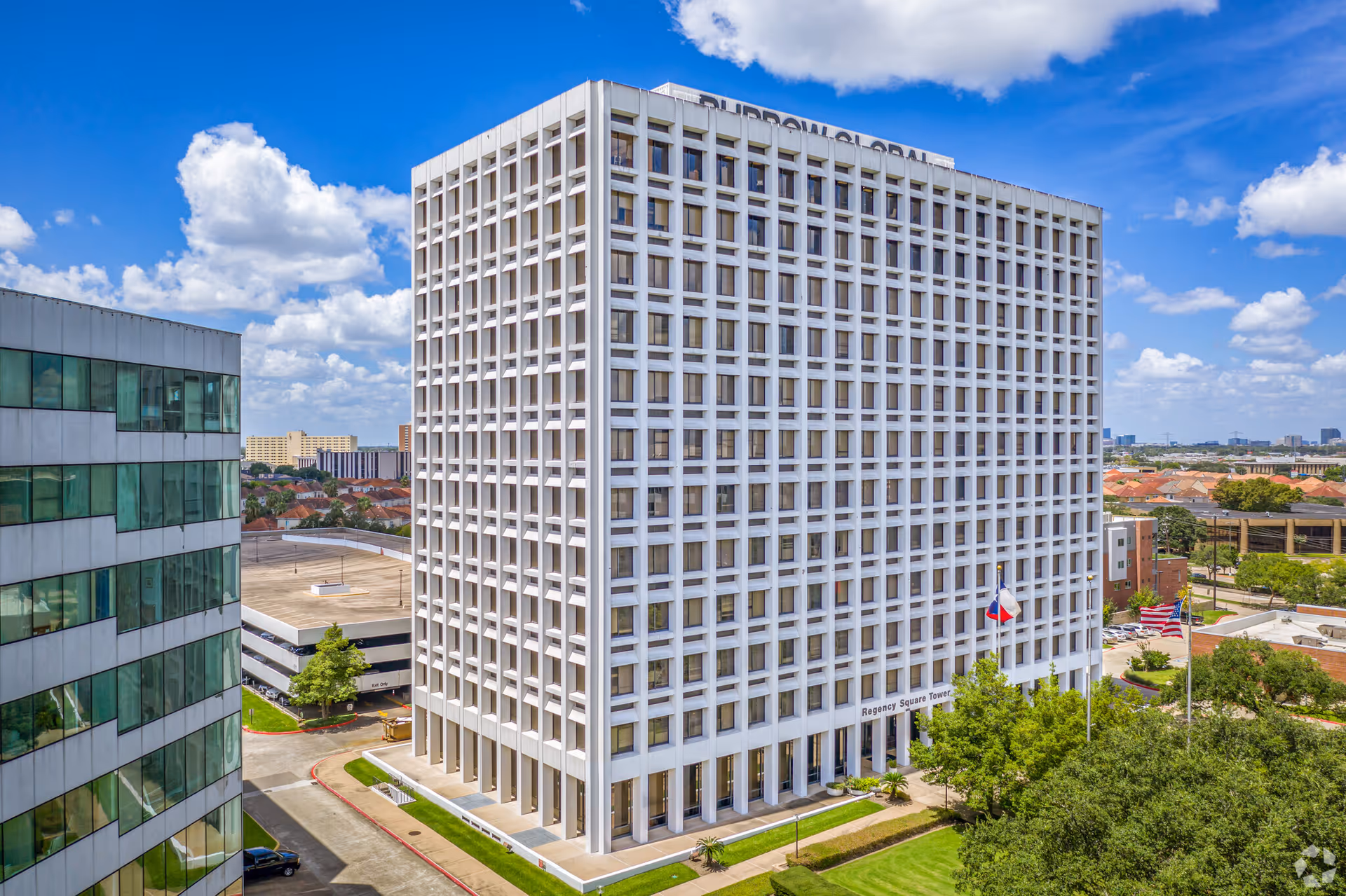 A tall white grid-windowed office tower with surrounding cityscape.