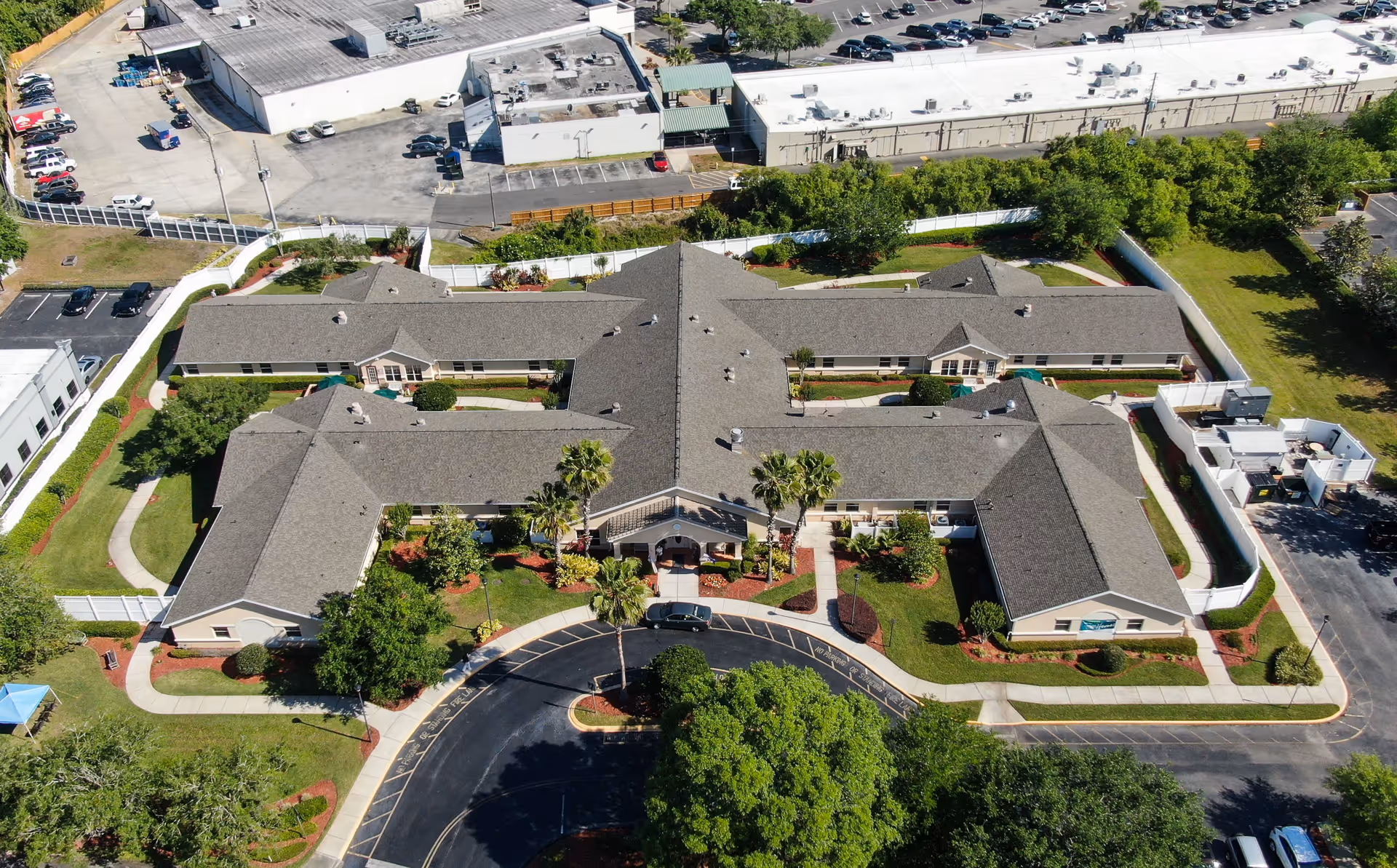 Aerial view of Arden Courts - ProMedica Memory Care Community in Winter Springs, showing a large, single-story building with a U-shaped layout surrounded by landscaped greenery, trees, and parking areas.