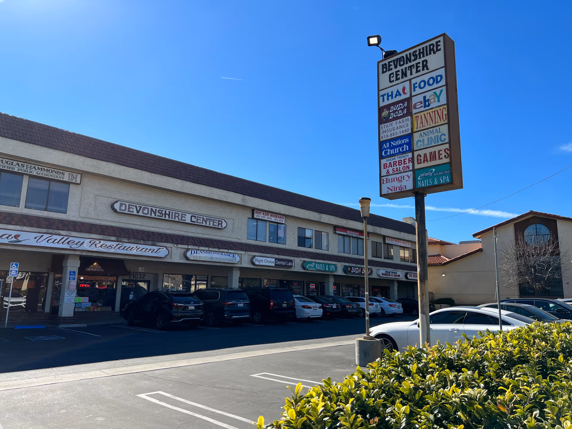 Front exterior of a strip mall with Devonshire Center signage and parked cars.