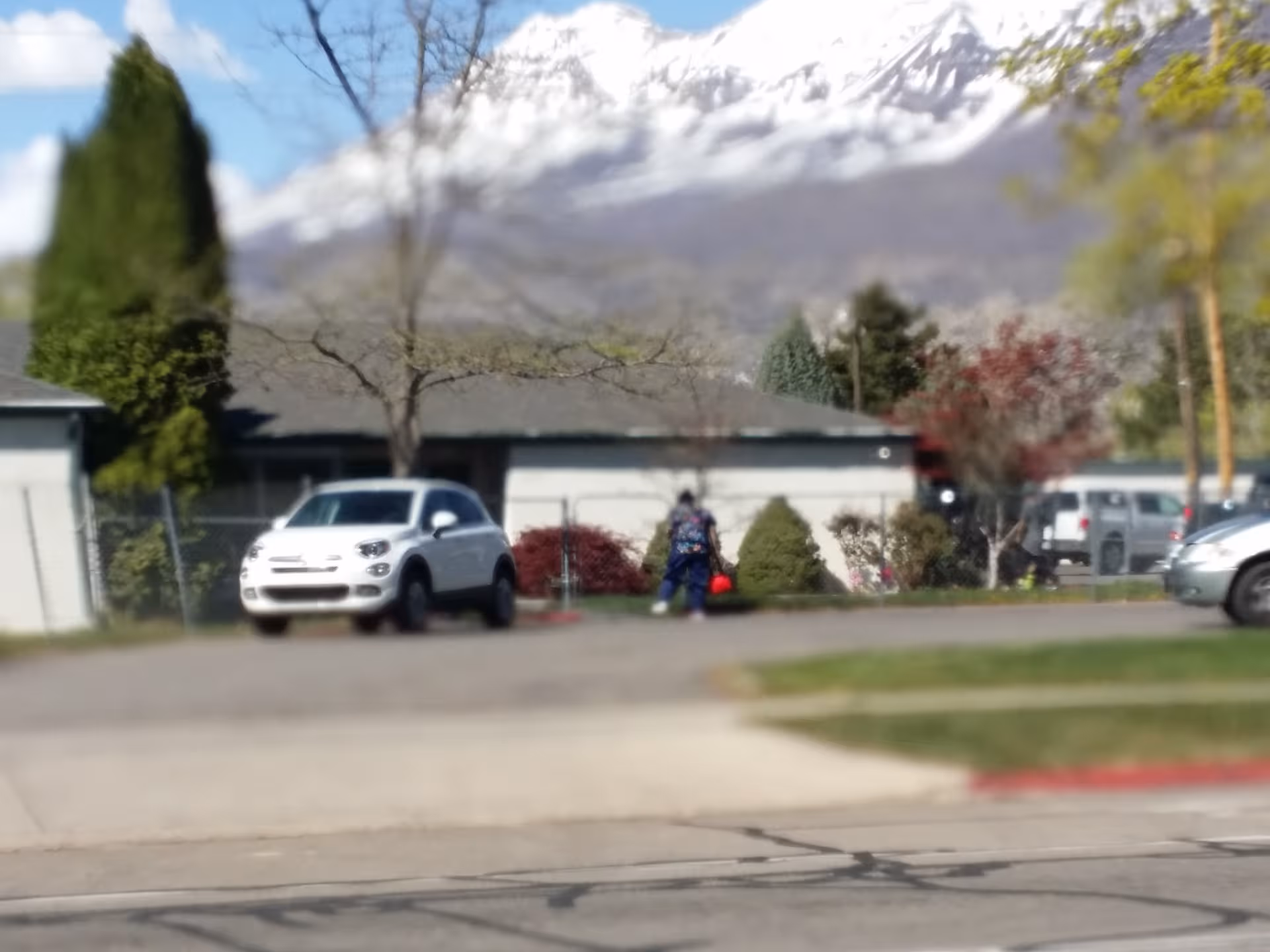 Exterior view of a senior living facility with parked cars and mountains in background.