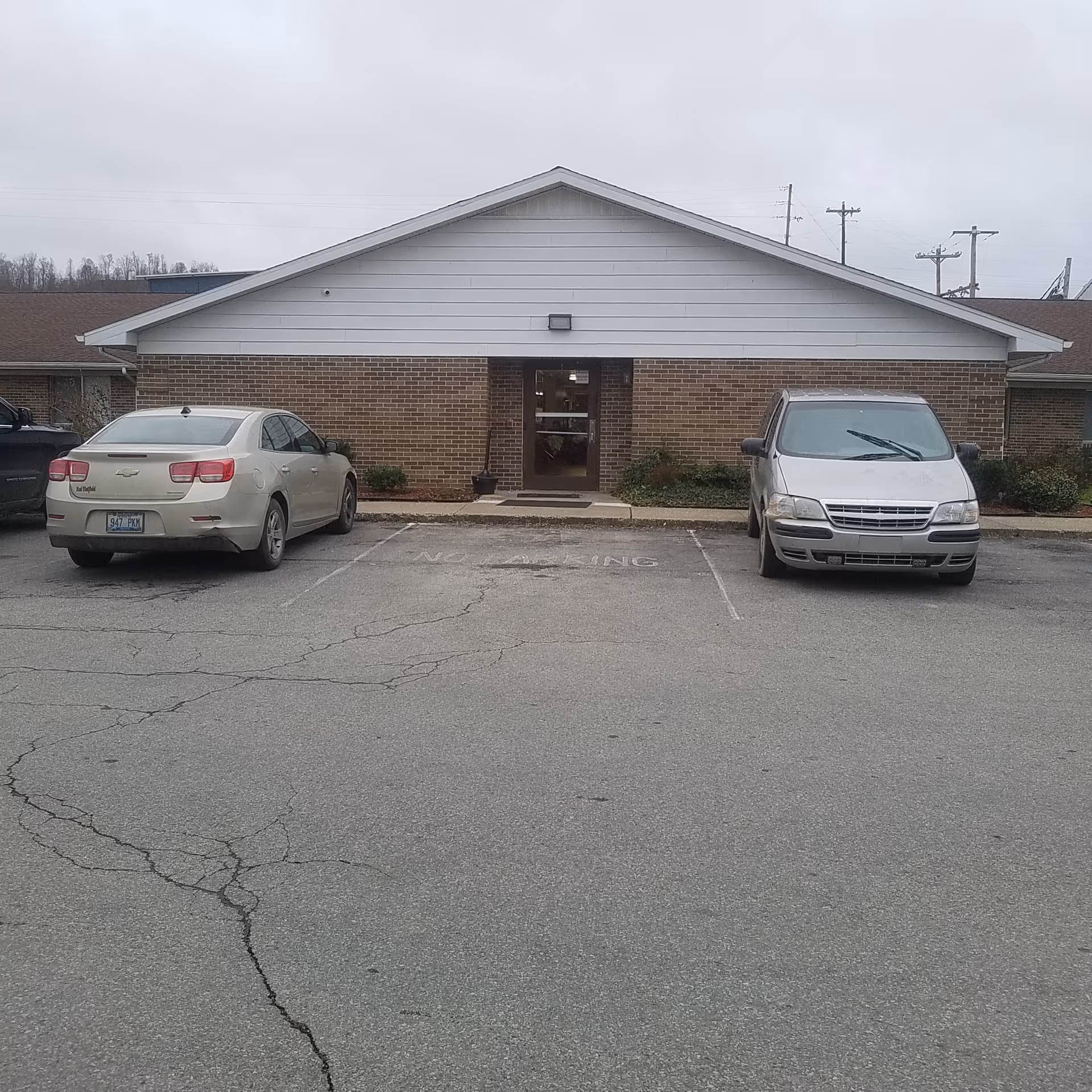 Brick-and-white single-story facility with central entrance and two parked cars.