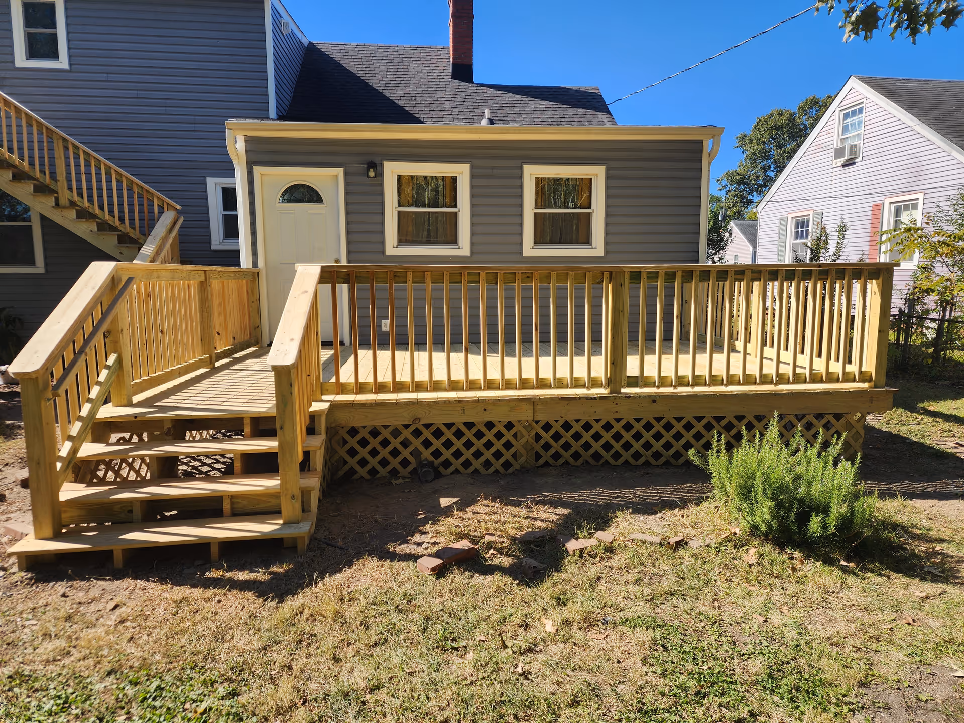 Wooden elevated deck attached to a gray house with stairs and railing.