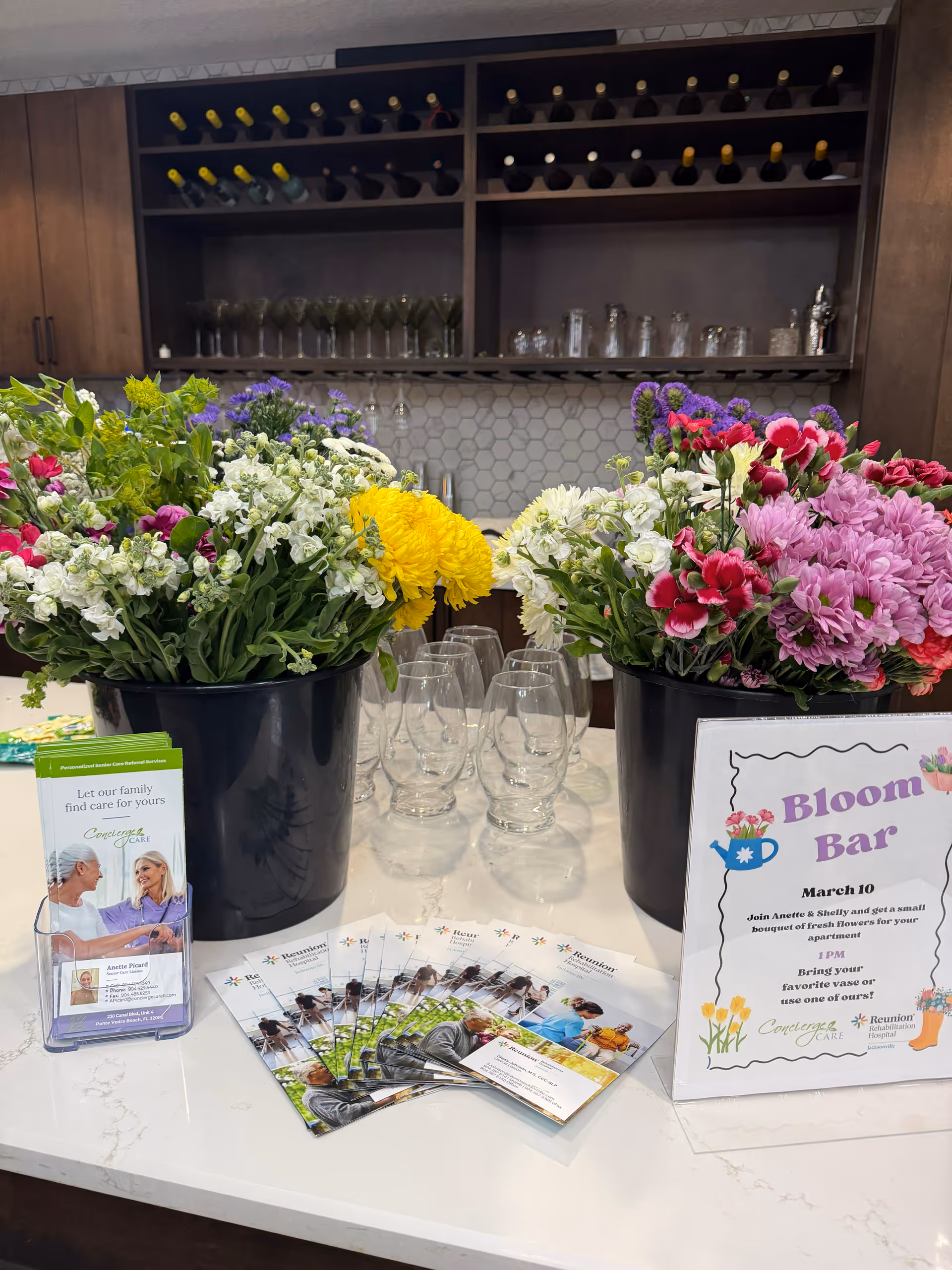 Flower-filled counter with glassware and a Bloom Bar sign in a concierge area.