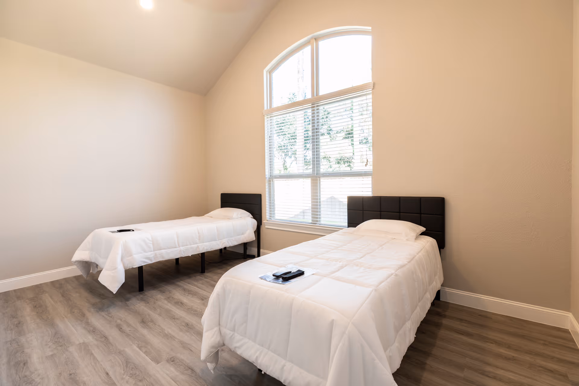 Two single beds with white quilts in a bright, minimalist senior living facility bedroom.