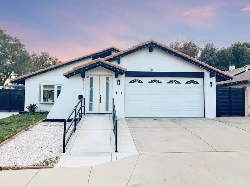 White single-story home with a two-car garage, front ramp, and neatly landscaped walkway.