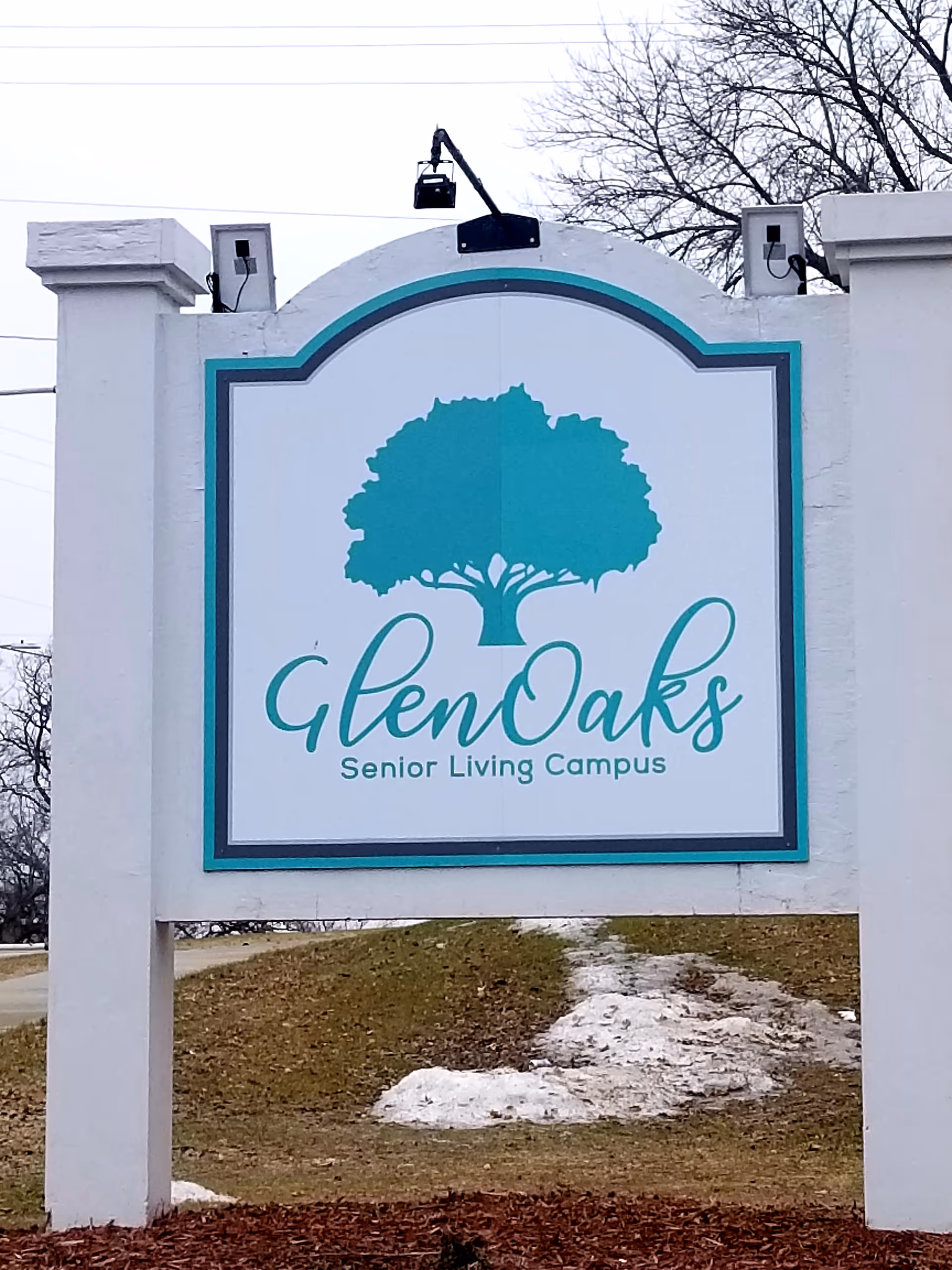 Exterior sign for GlenOaks Senior Living Campus featuring teal tree logo and border.