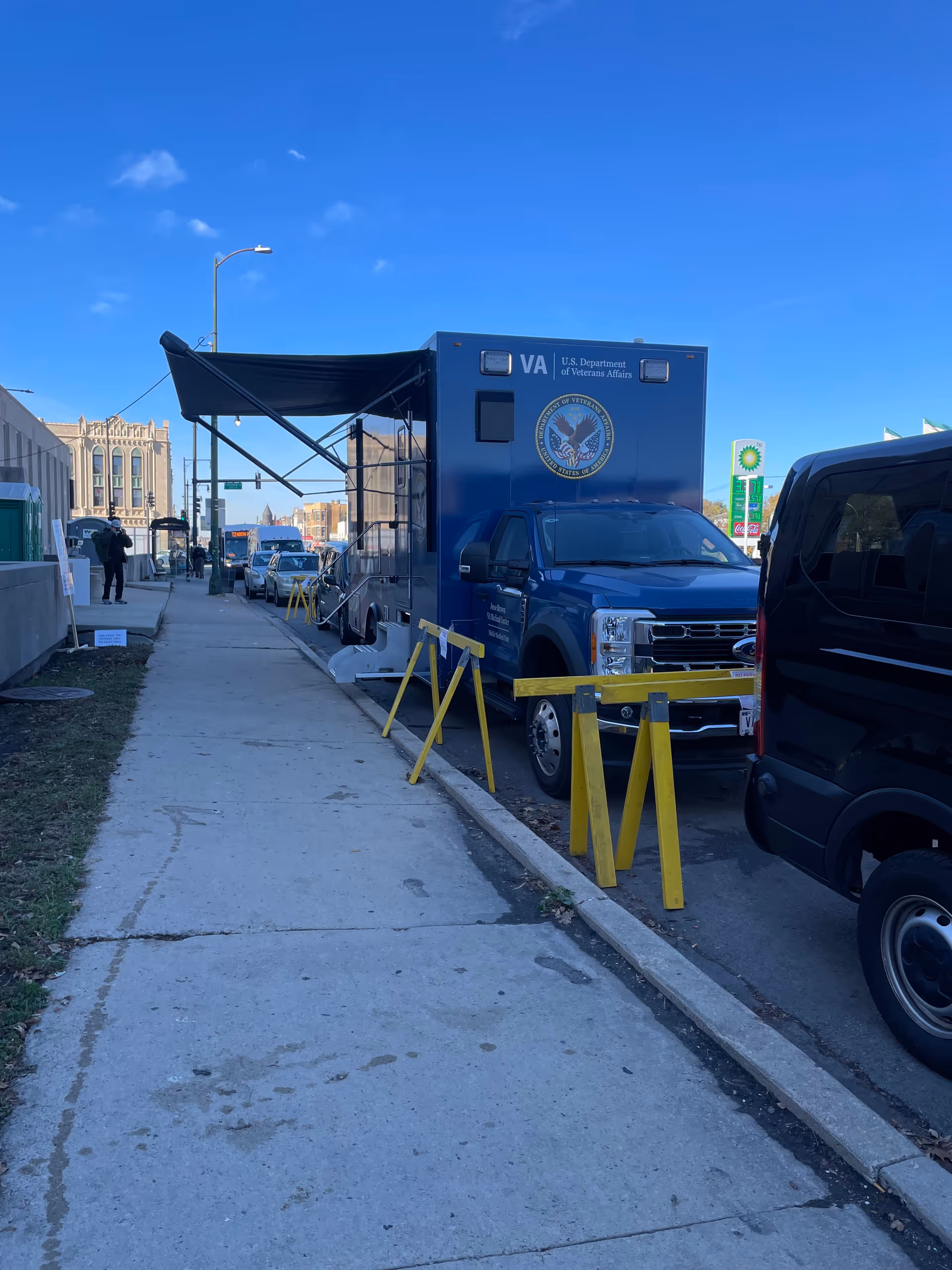 Blue VA mobile clinic truck parked beside a sidewalk with yellow safety barriers.