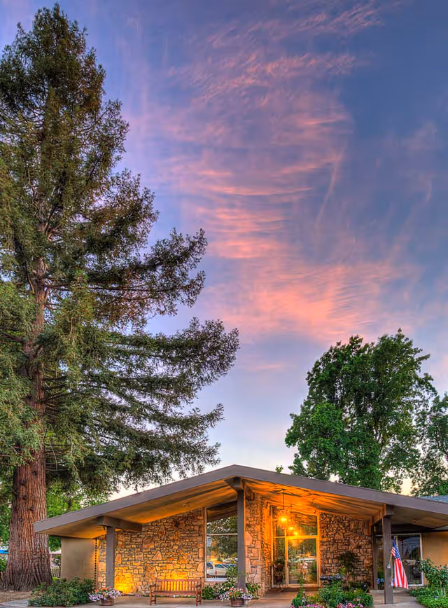 Single-story stone-faced senior living facility front entrance at sunset.