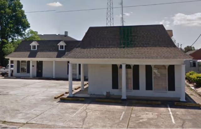 Single-story white brick building with columns and a front parking lot.