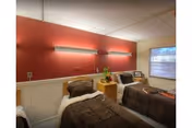Two single beds with brown bedding in a red-accented shared bedroom, window on the right.