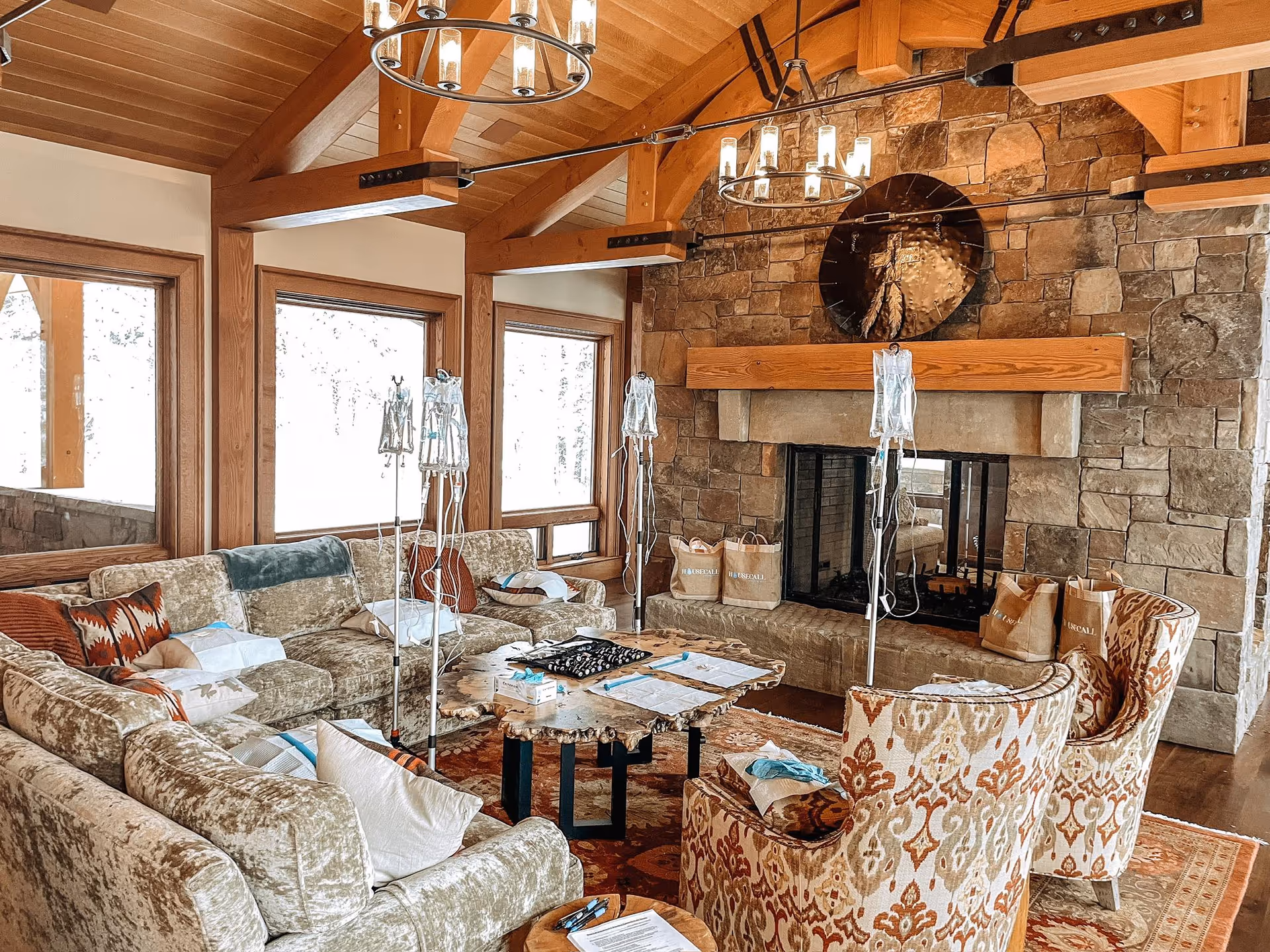 Cozy lodge-style living room with stone fireplace, plush seating, chandeliers, and IV drip poles.