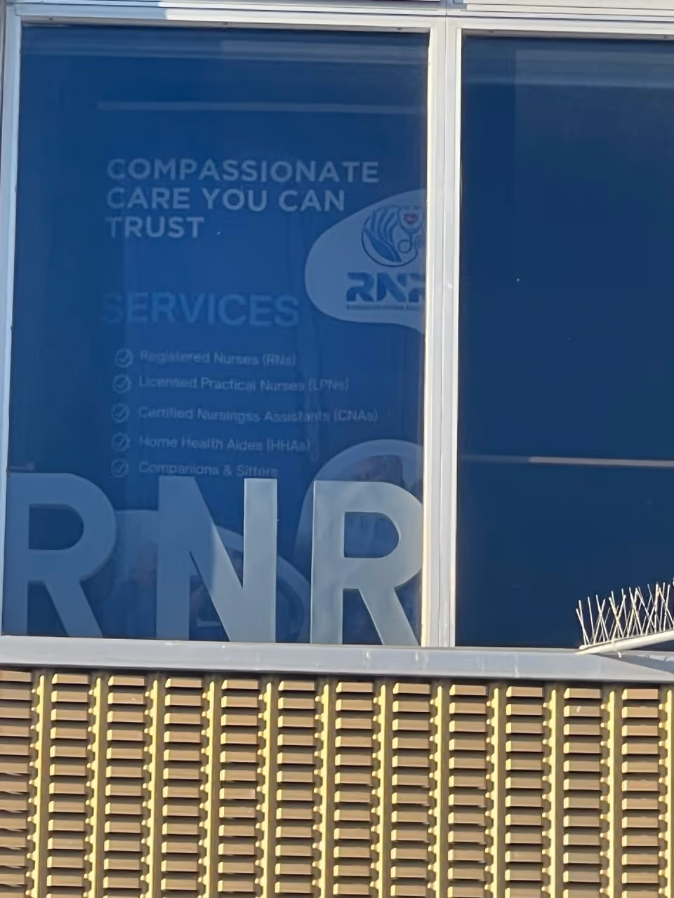 Blue-tinted window signage advertising compassionate care and RN registry on building front