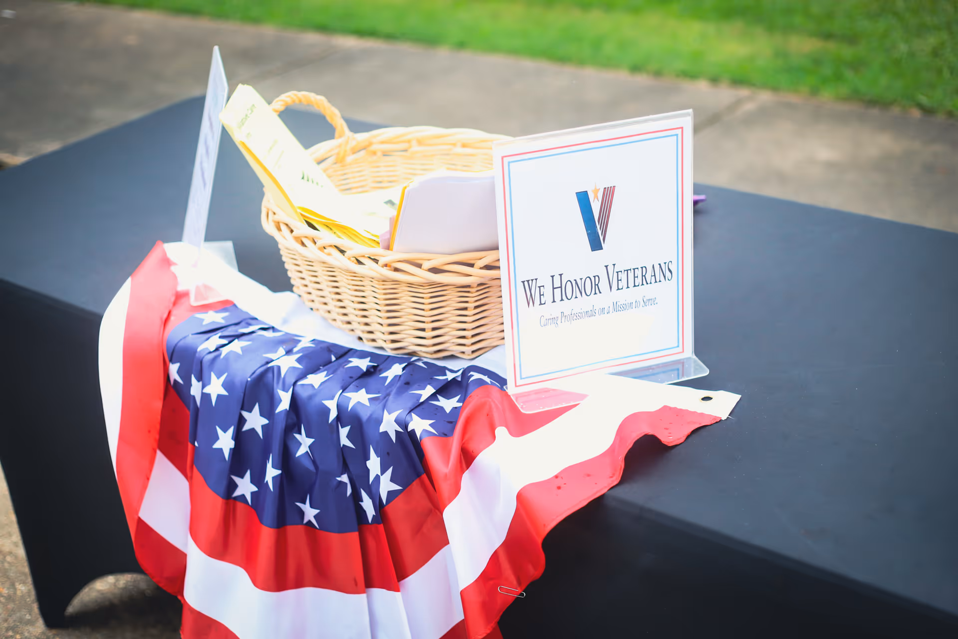 Outdoor table with American flag cloth, basket, and 'We Honor Veterans' sign on display.