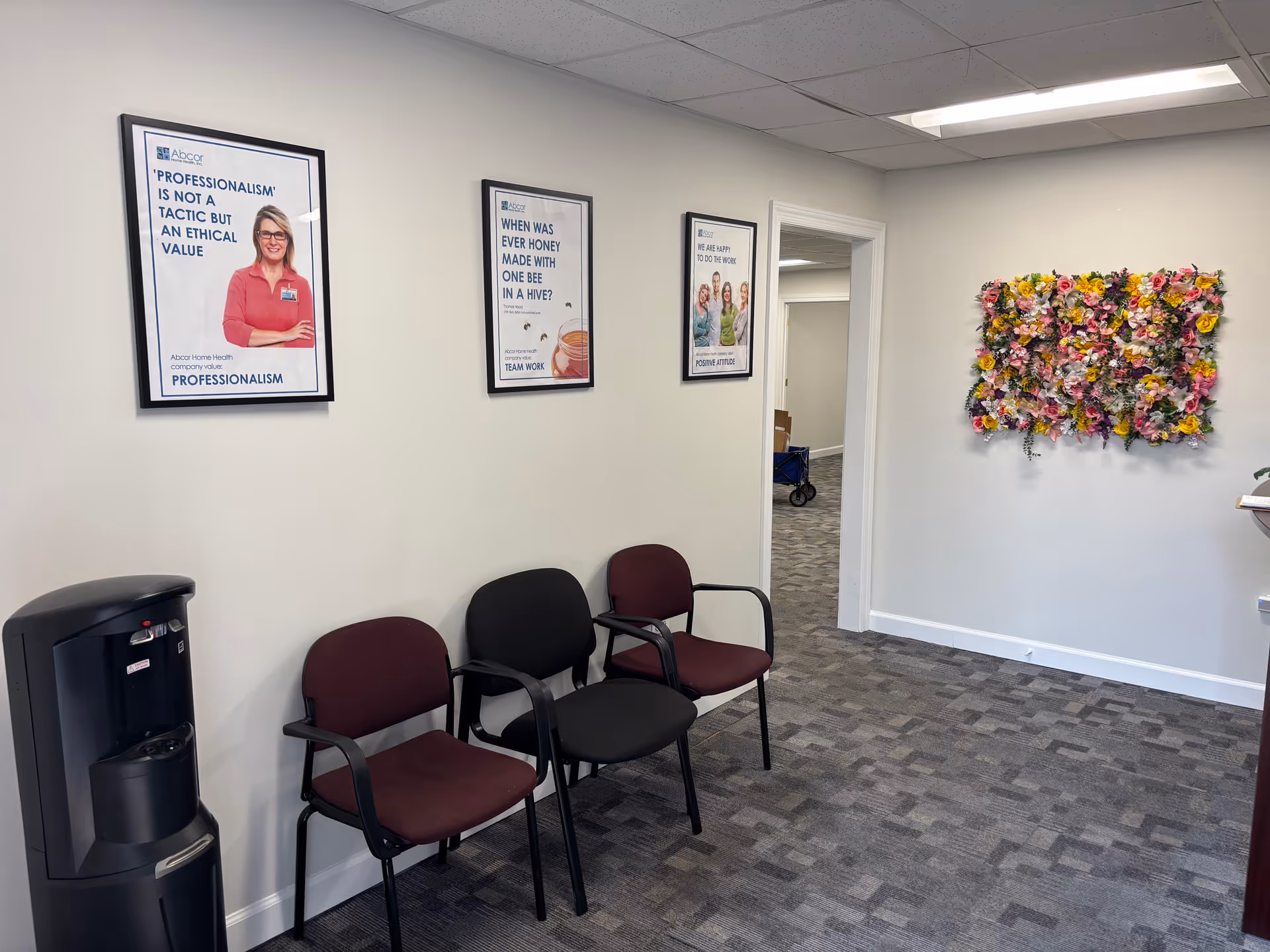 A waiting area with four chairs, water cooler, framed posters, and floral wall decor.