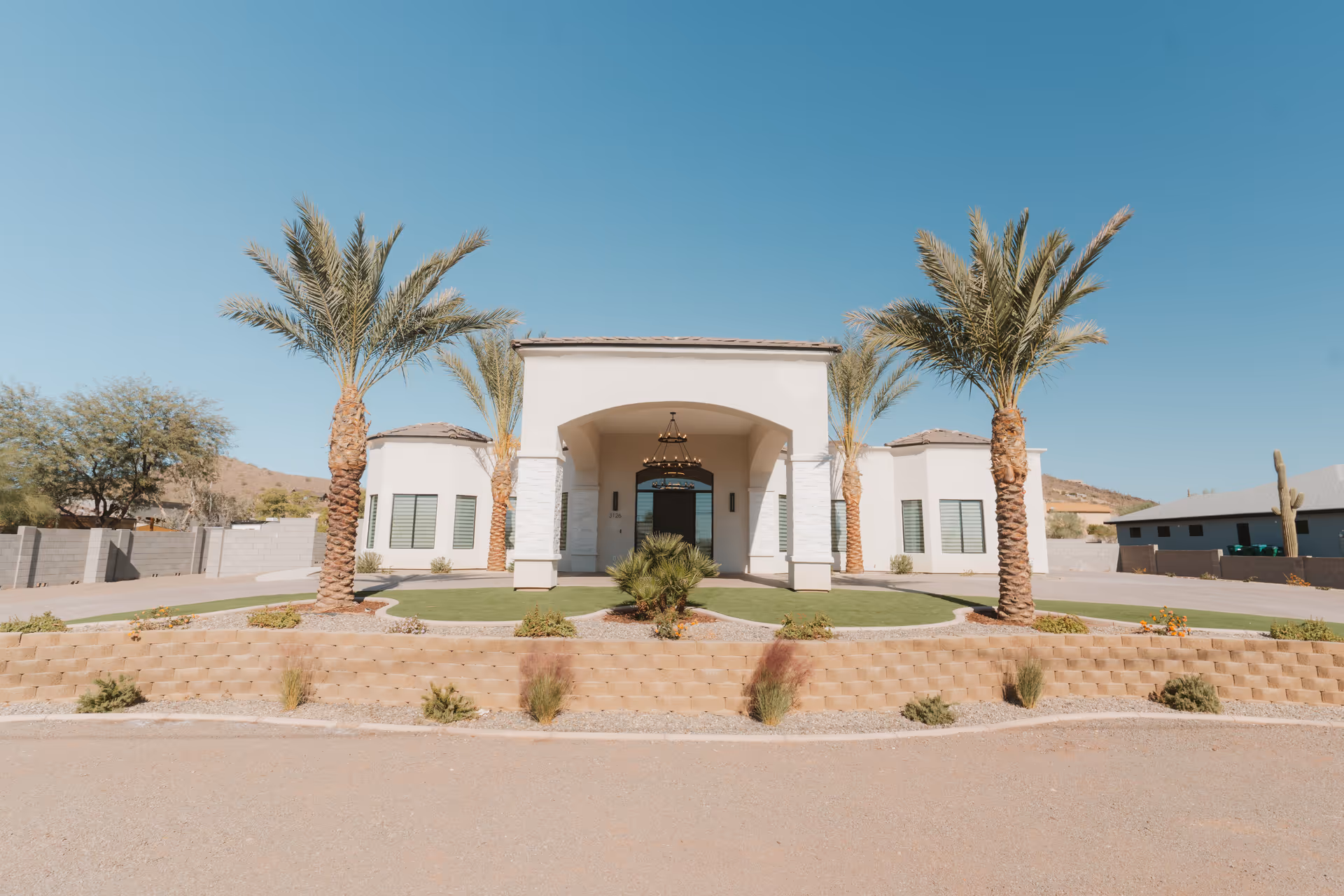 Front view of a white Deer Valley Care Home building with palm trees and desert landscaping