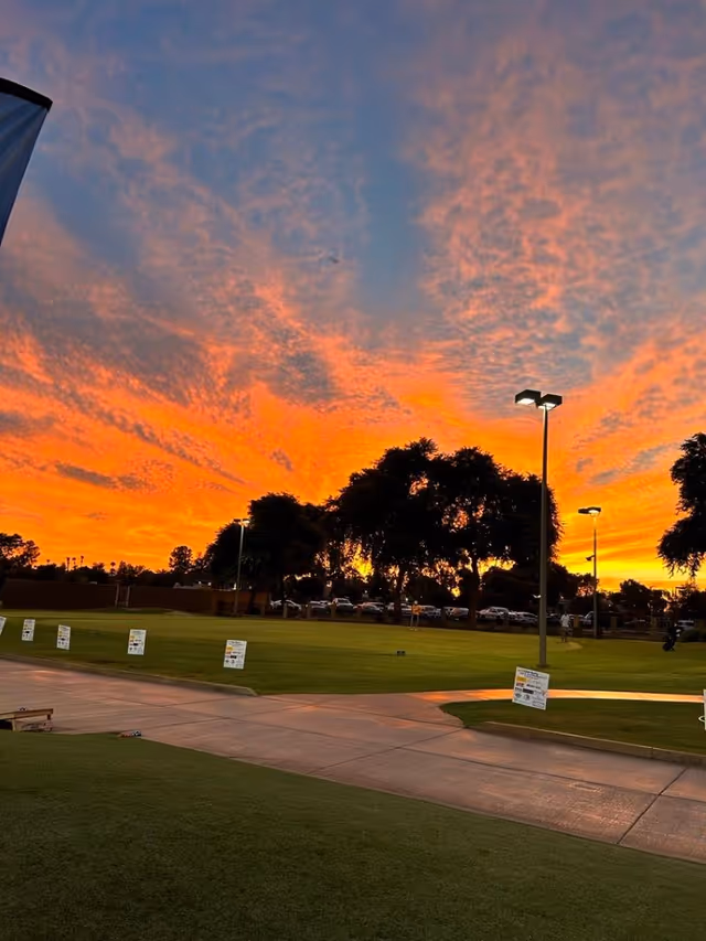 Sunset sky over a grassy outdoor area with walkways and street lamps.