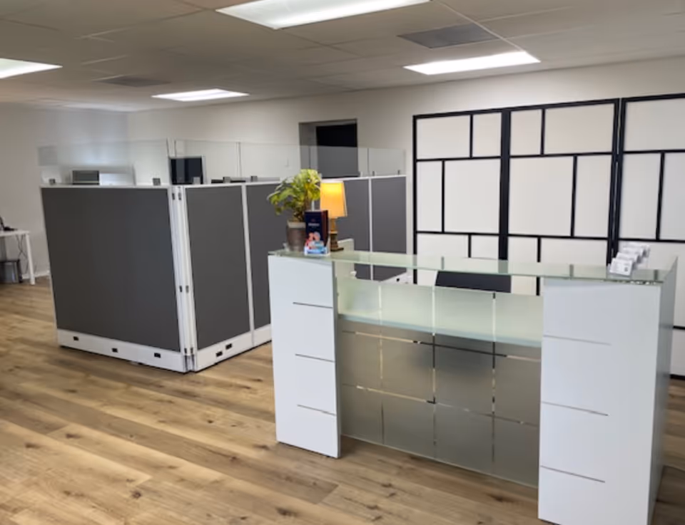 Reception desk in a modern, office-like lobby with partition walls and wood flooring.