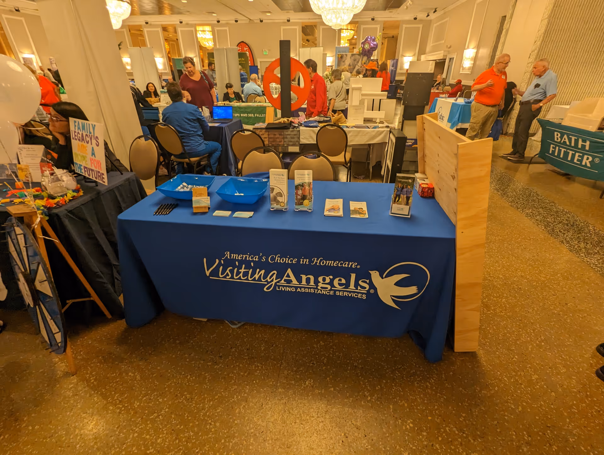 Indoor expo hall featuring Visiting Angels Senior Home Care booth with attendees and displays.