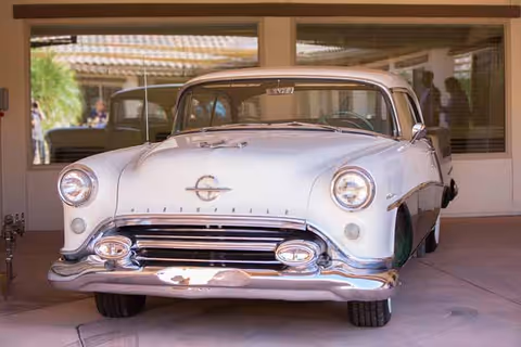 A vintage white car parked under a covered entryway in front of a building.