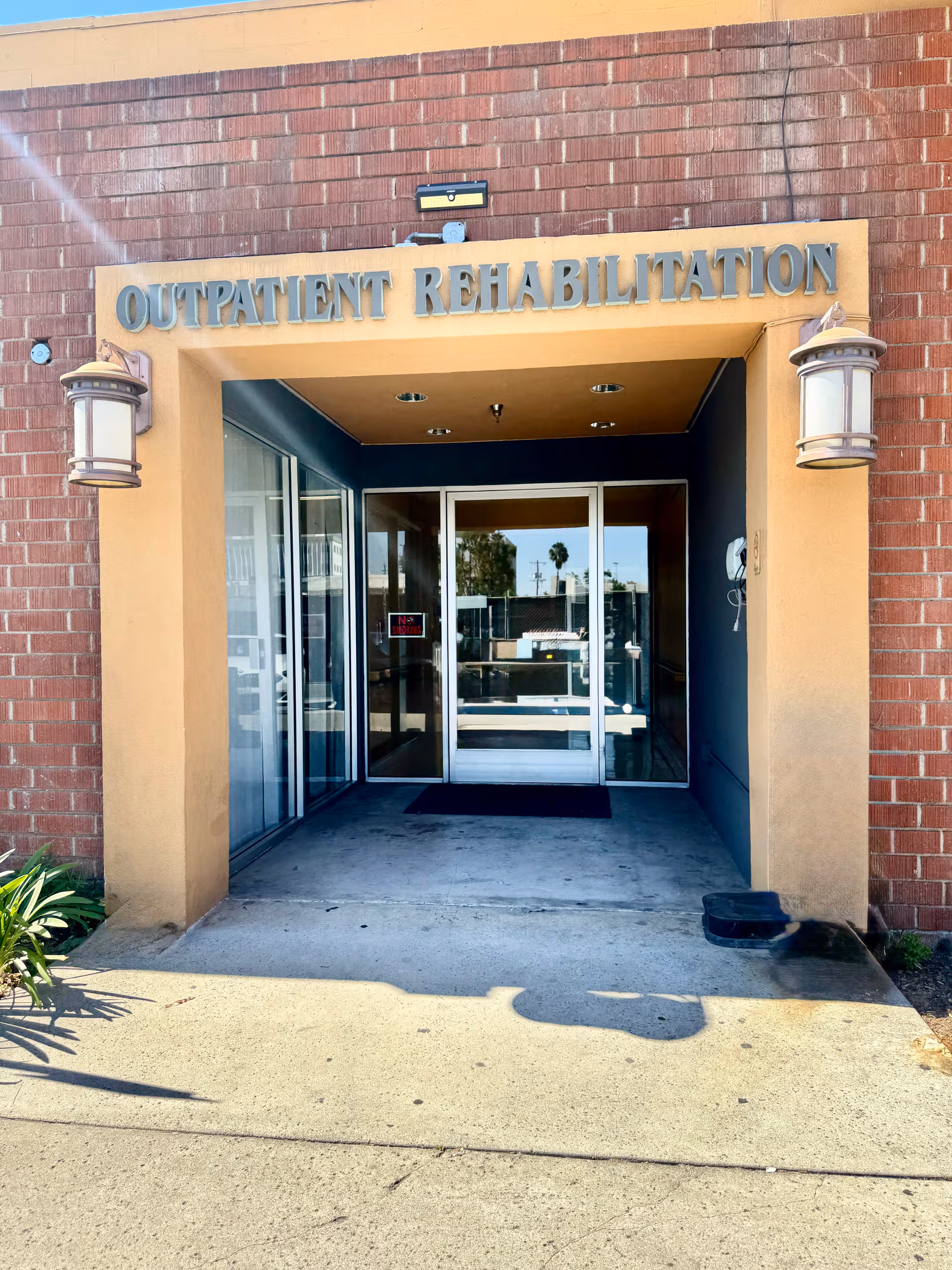 Brick exterior entrance with glass doors labeled Outpatient Rehabilitation, under a brick facade.