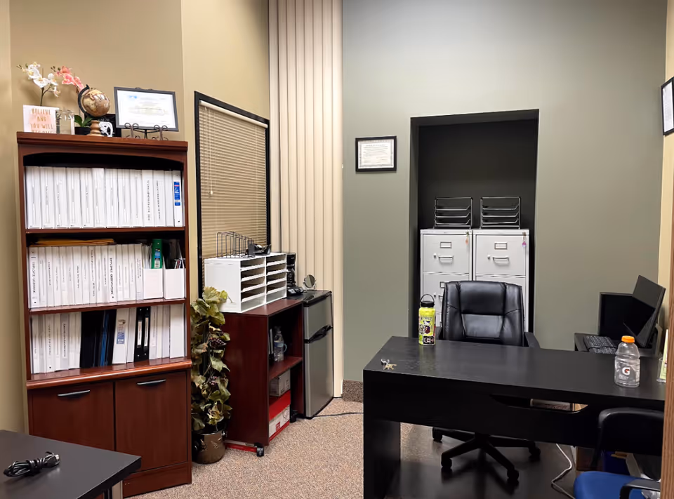 Office workspace with desk, filing cabinets, and shelves of binders.