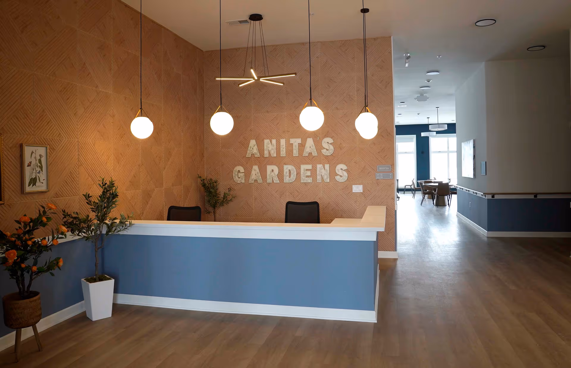 Reception desk in Anita's Gardens lobby with geometric wall, plants, and seating.