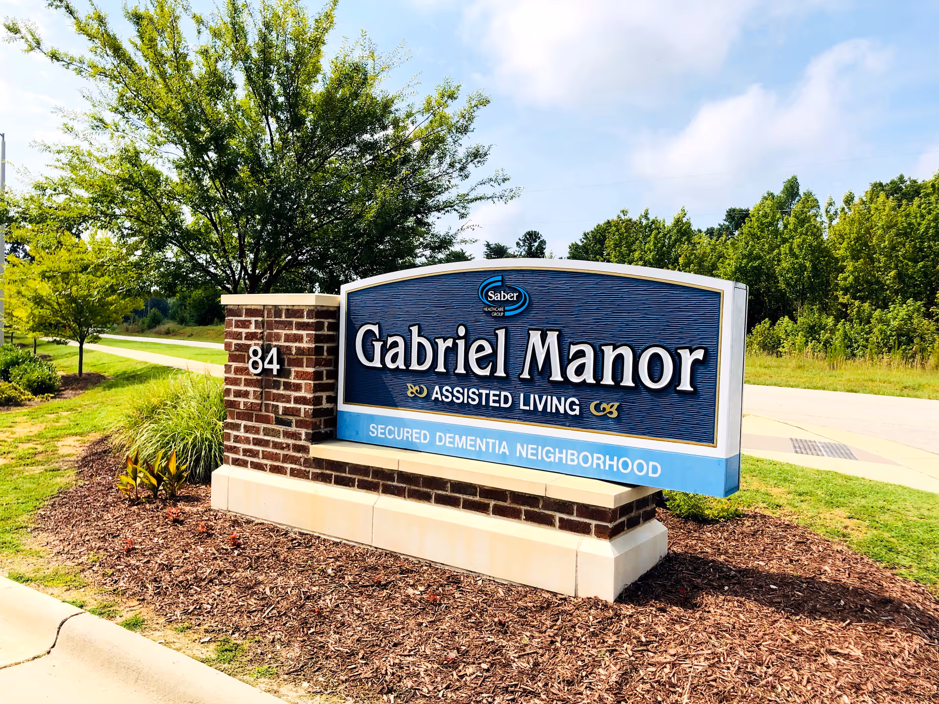 Gabriel Manor Assisted Living sign on brick pedestal in landscaped outdoor space.