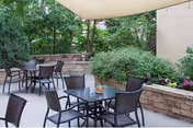 Outdoor patio with tables, chairs, umbrellas, and greenery outside Burlington Health & Rehab.