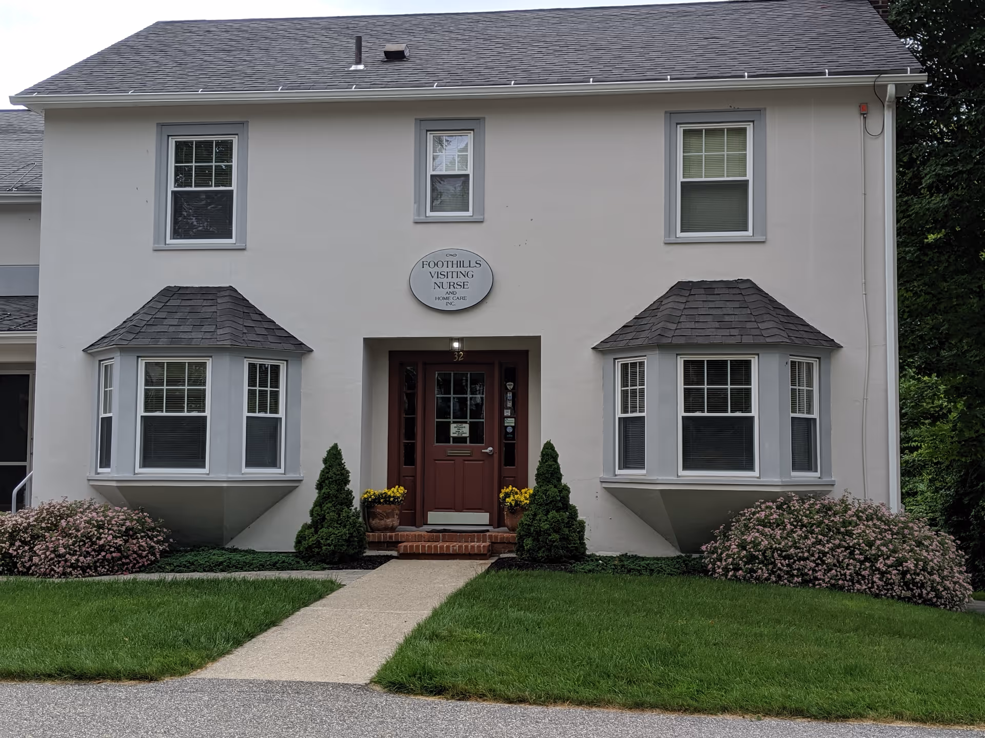 Two-story beige building with Foothills Visiting Nurse sign, red door, and landscaped lawn.