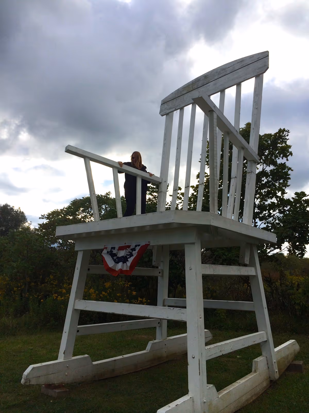 A tall white lifeguard-style chair outdoors with a person standing on the railing.