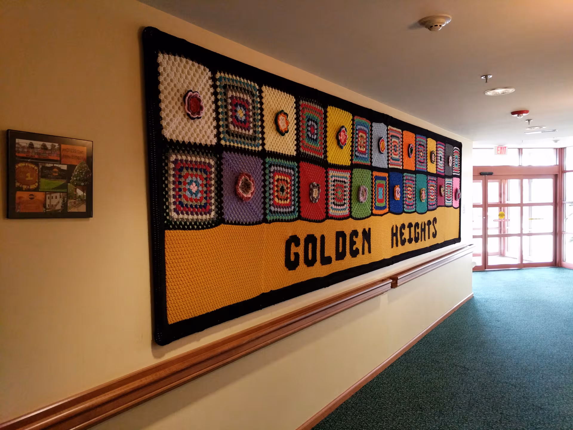 Colorful crocheted wall quilt with GOLDEN HEIGHTS along a hallway in a senior facility.