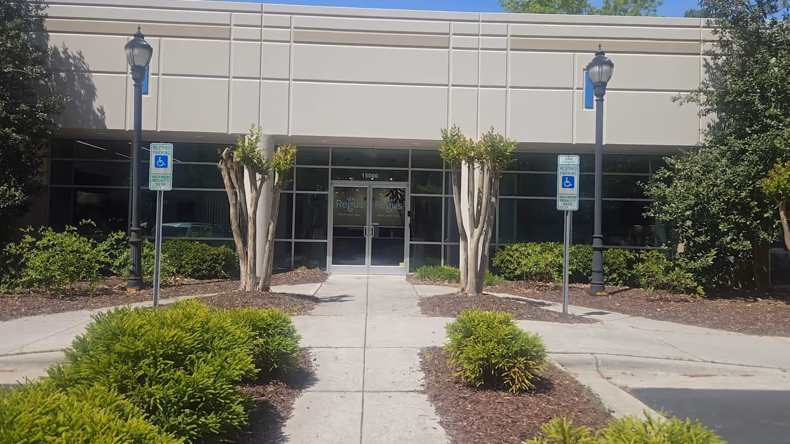 Front exterior view of a beige building with glass entrance and landscaped walkway.