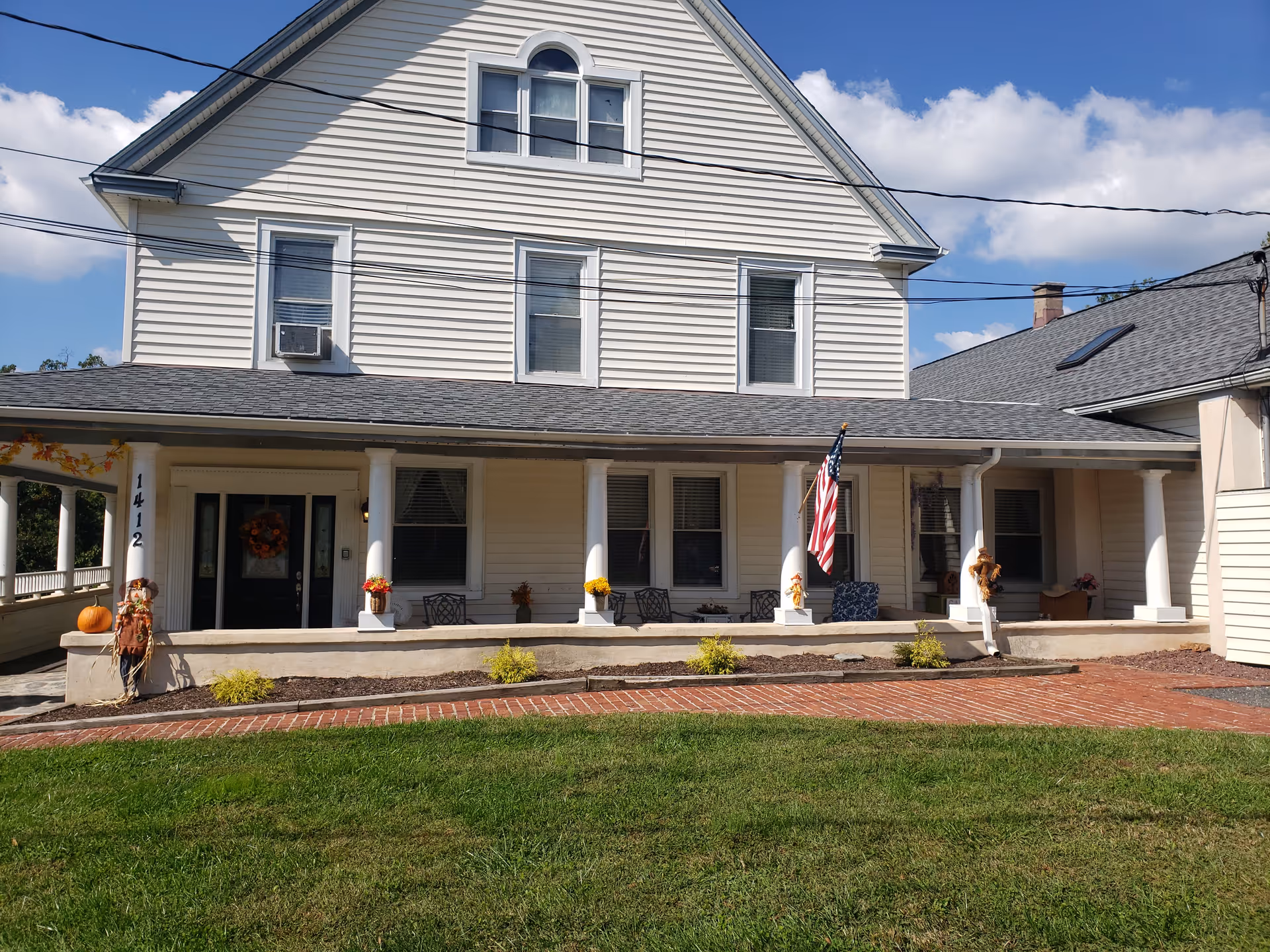 White two-story assisted living home with a spacious front porch, columns, and an American flag.