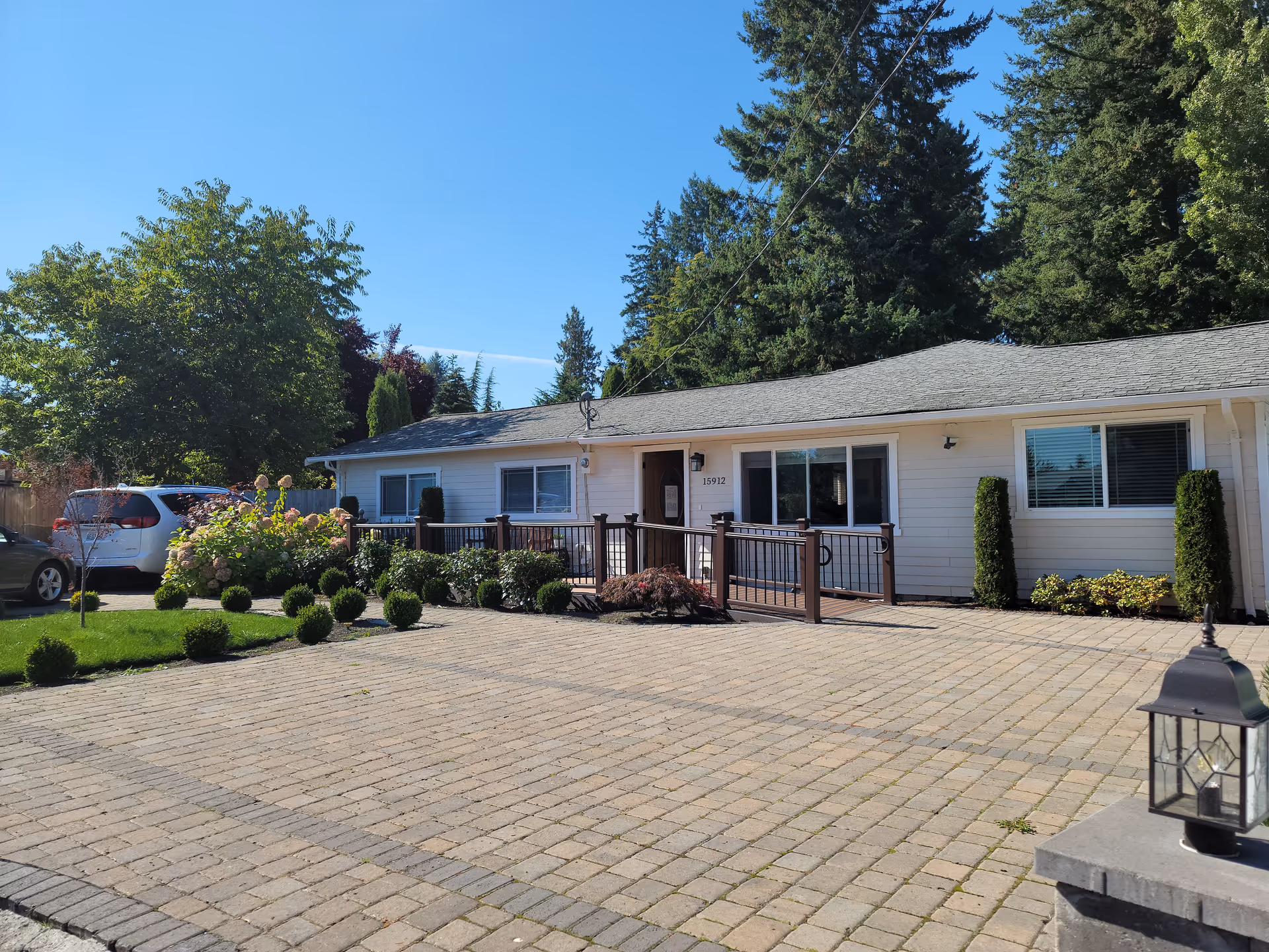 Single-story beige senior home with a ramp, manicured shrubs, and a paved driveway.