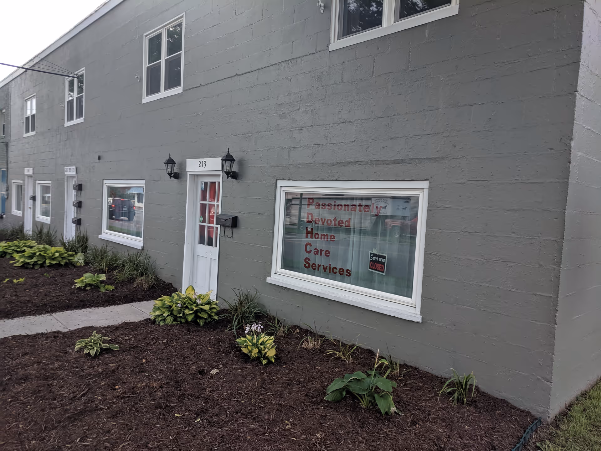 Grey exterior building with white door and window sign for Passionately Devoted Home Care Services.