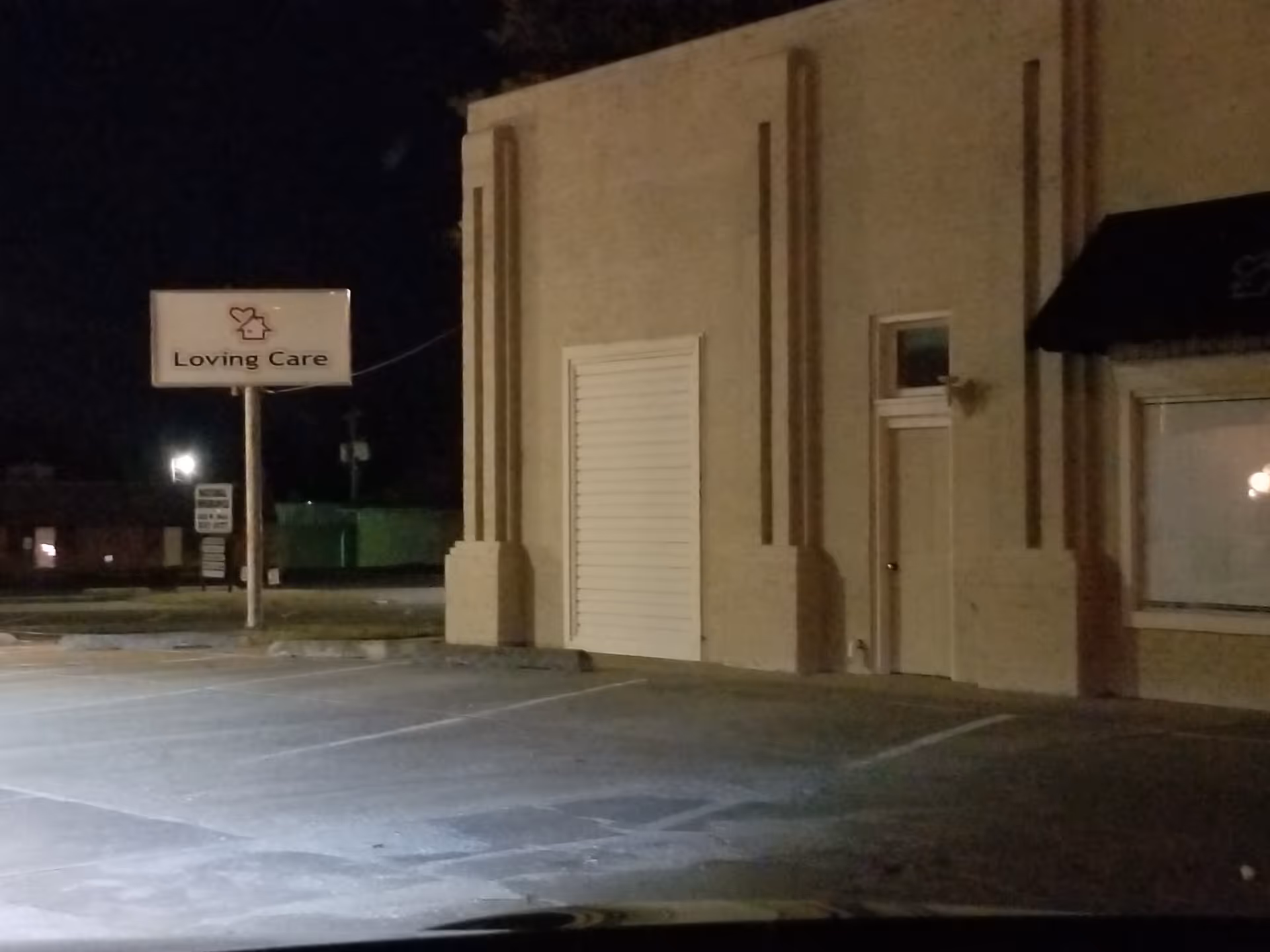Nighttime exterior of a beige building with a Loving Care sign on the front.