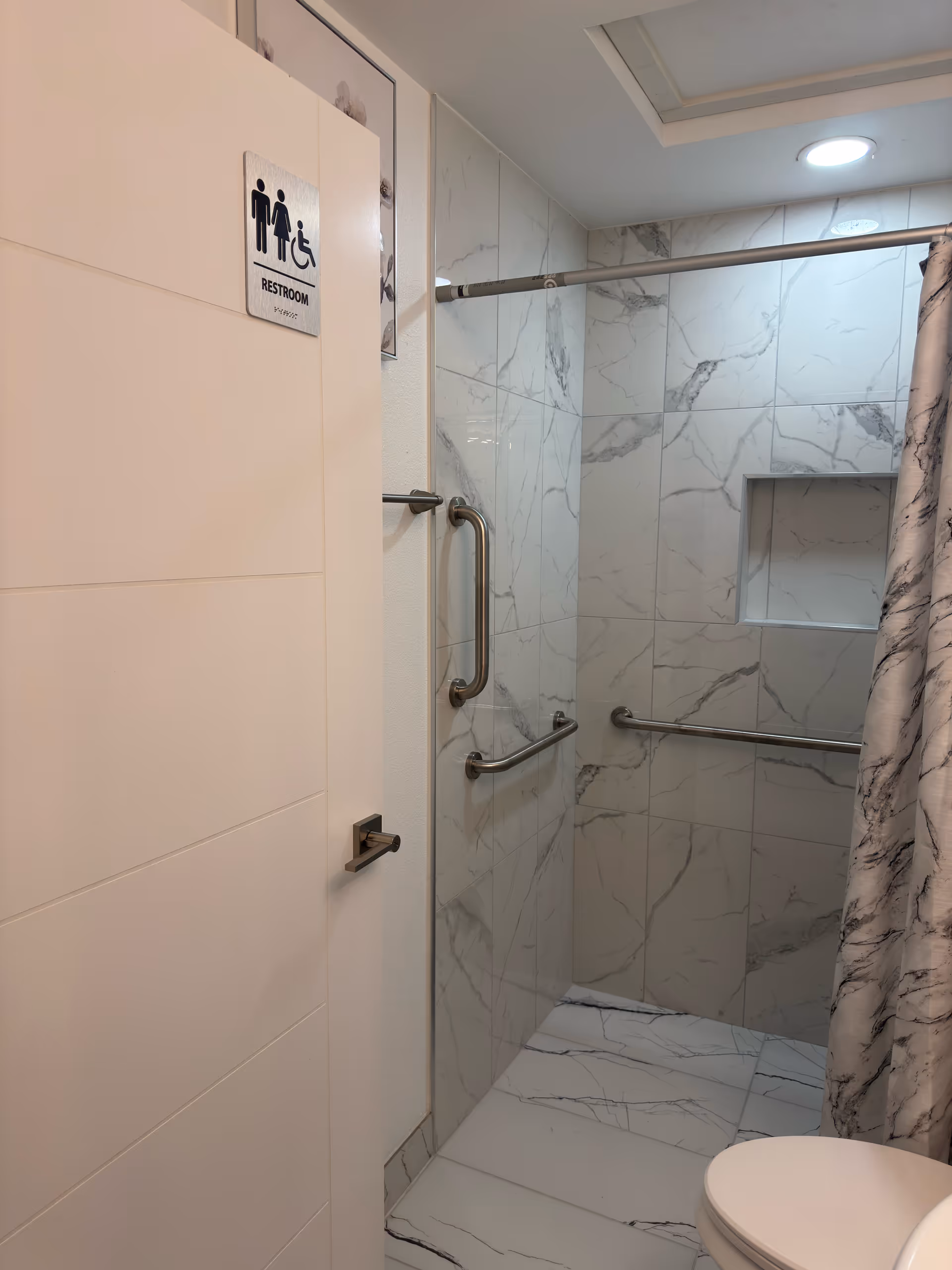 Marble-tiled bathroom interior featuring grab bars and a shower stall.