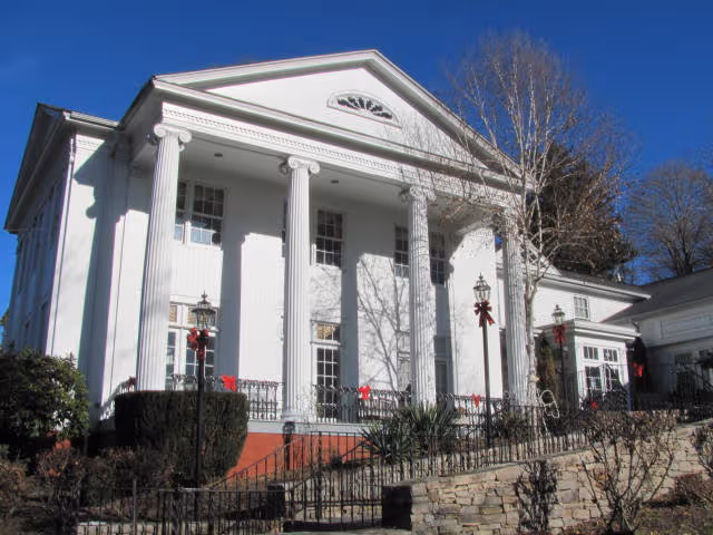 White classical-style building with columns, steps, and railings under a clear blue sky.