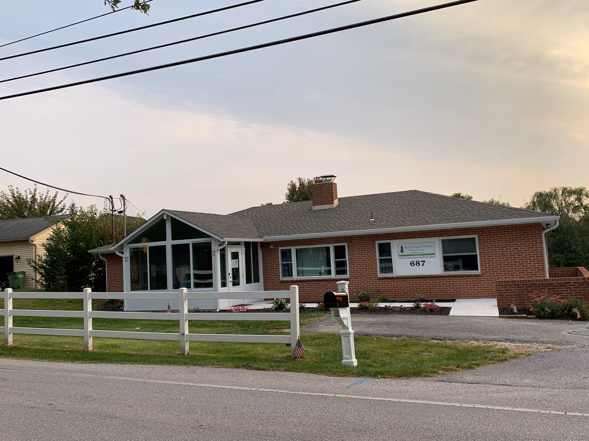 Brick senior living facility with glass-front entrance, white fence, and Pine Manor Home sign.