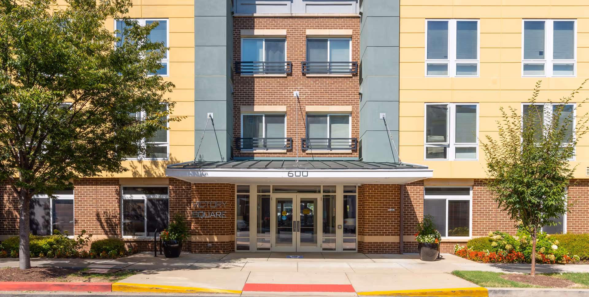 Exterior view of Victory Square Apartments entrance with brick and yellow facade.