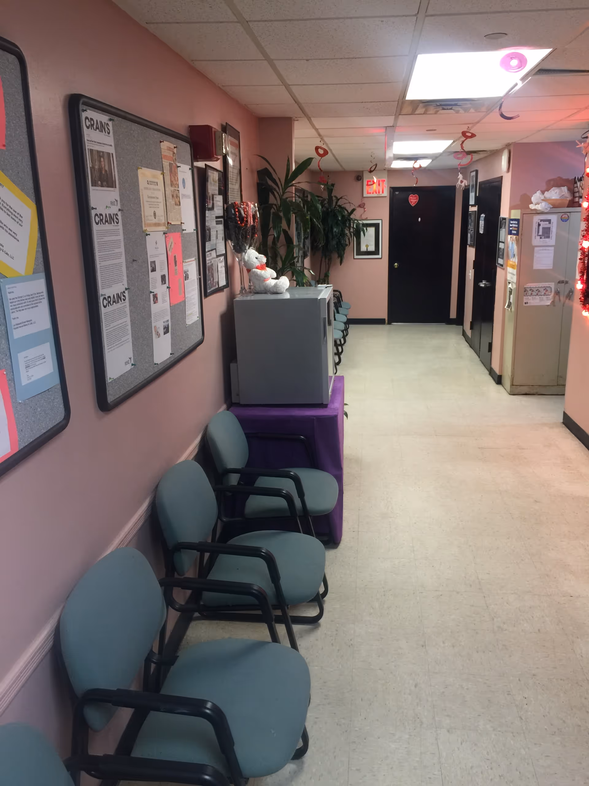Interior hallway of a senior facility with pink walls, bulletin boards, and chairs.
