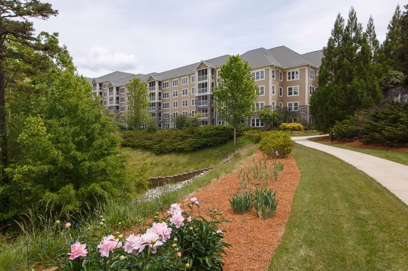 A multi-story senior living building sits along a curved walkway with landscaped grounds.