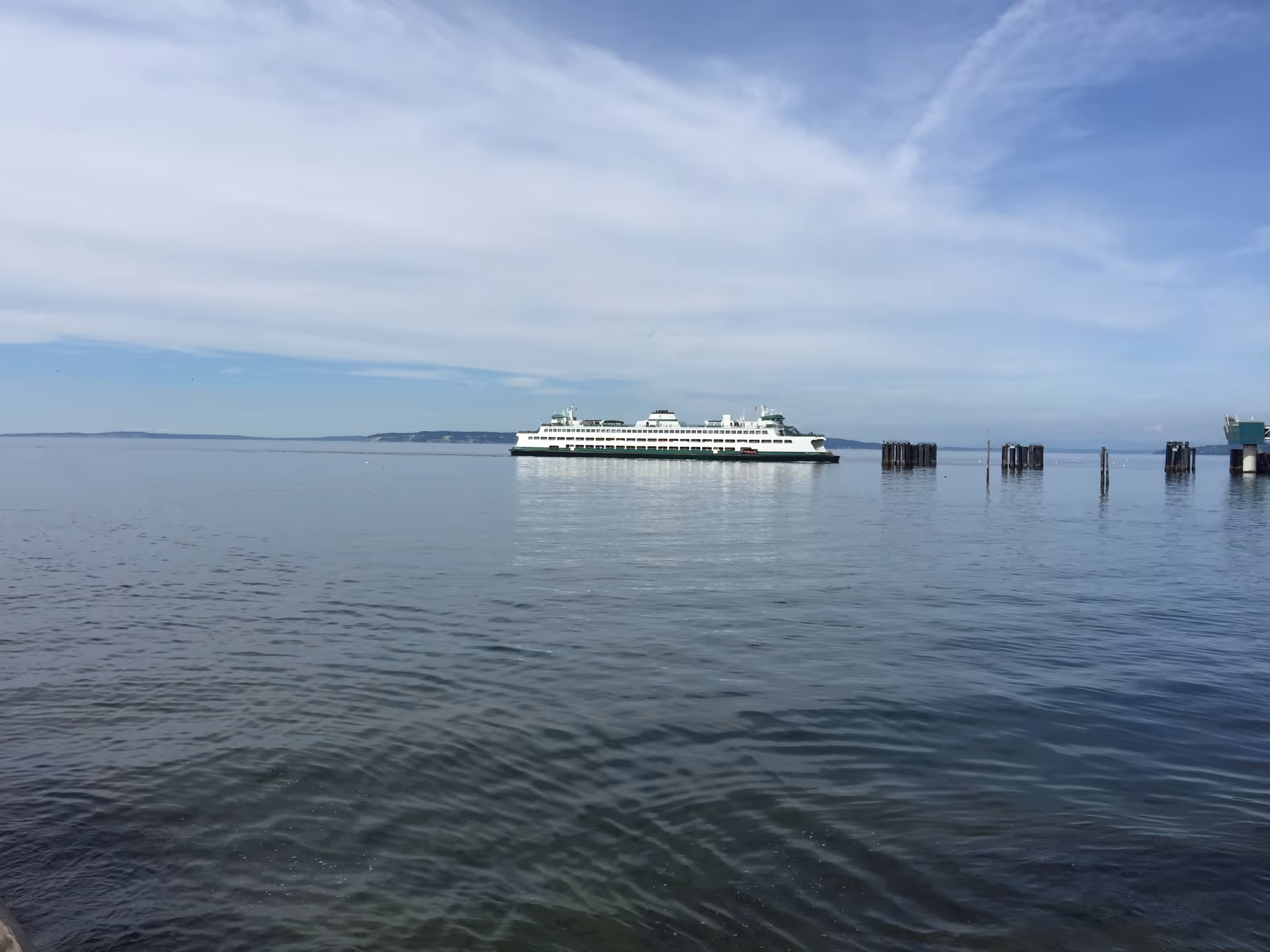 Calm sea with a white ferry sailing near a distant shoreline under blue sky.