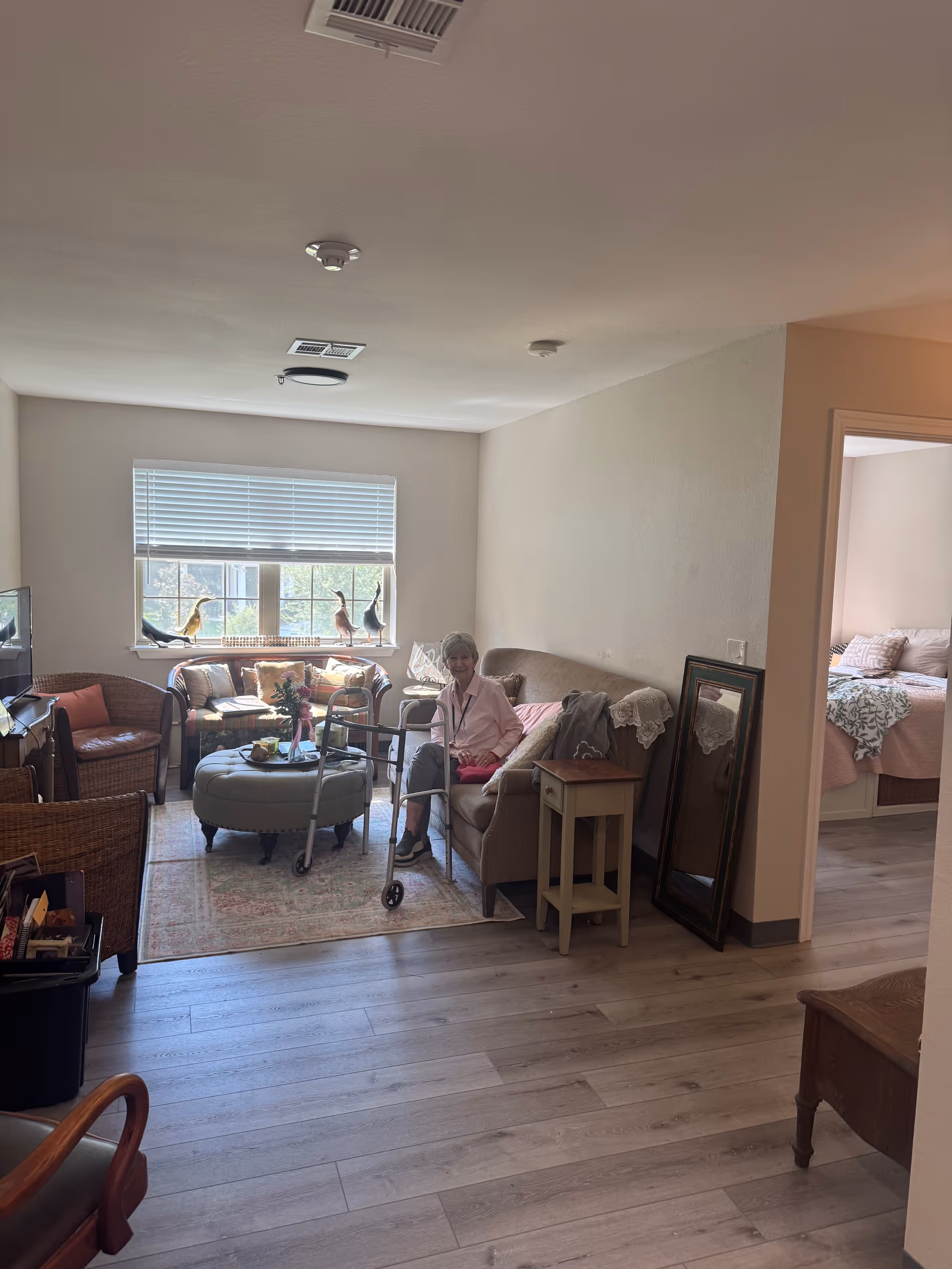 Elderly resident seated on a sofa in a cozy living room with a walker nearby.