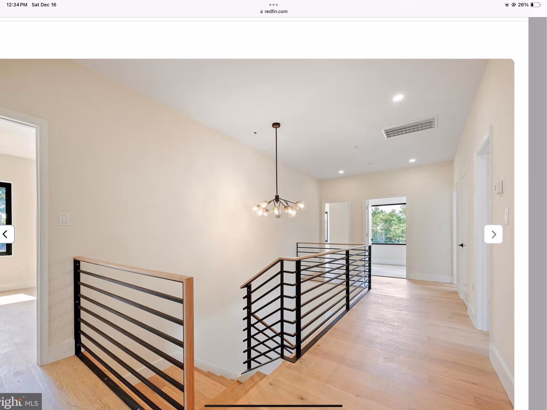 Bright modern upstairs hallway with wooden floor, metal railing, and a hanging light fixture.