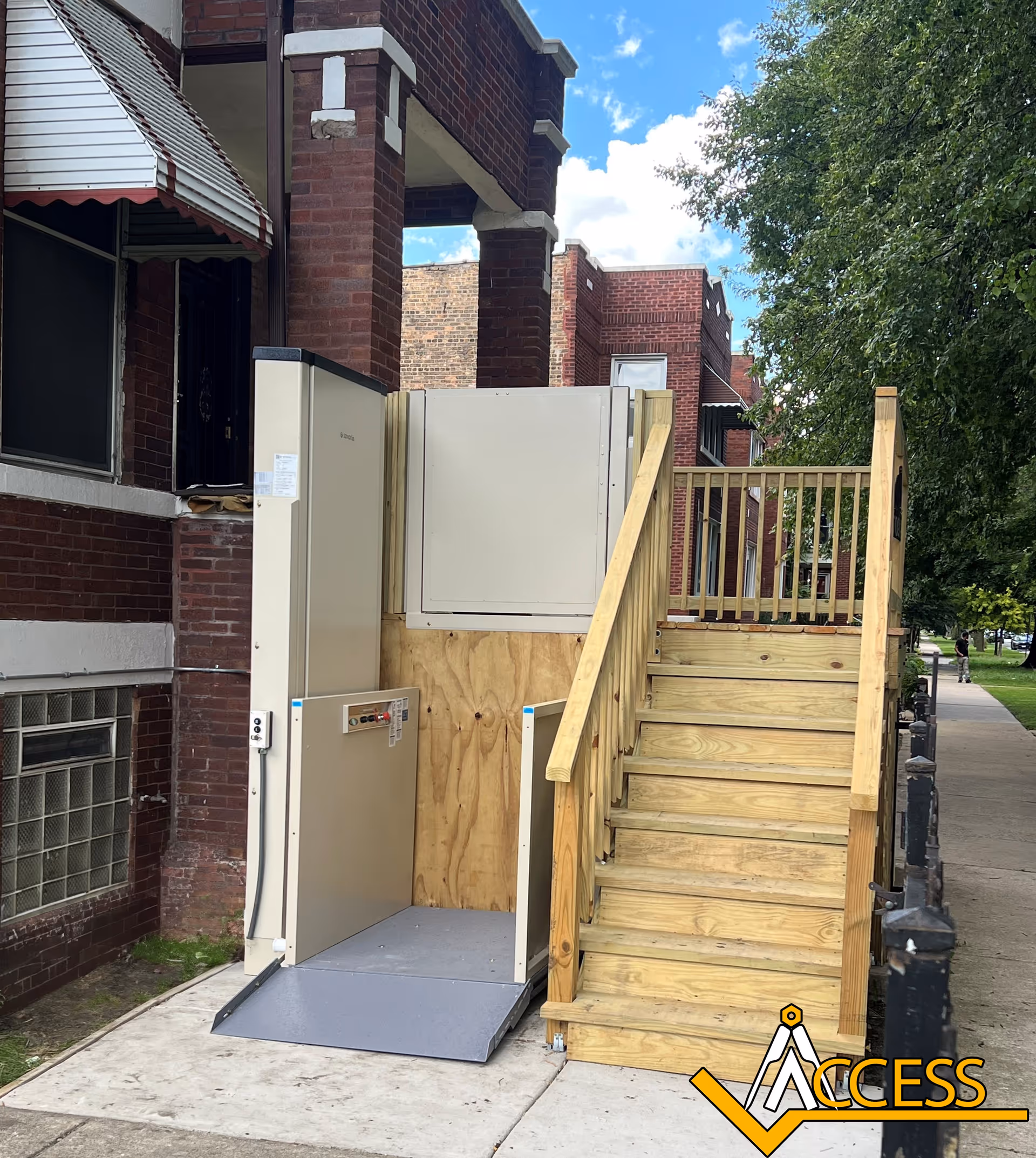 Outdoor accessibility elevator platform beside brick building with wooden stairs and raised deck
