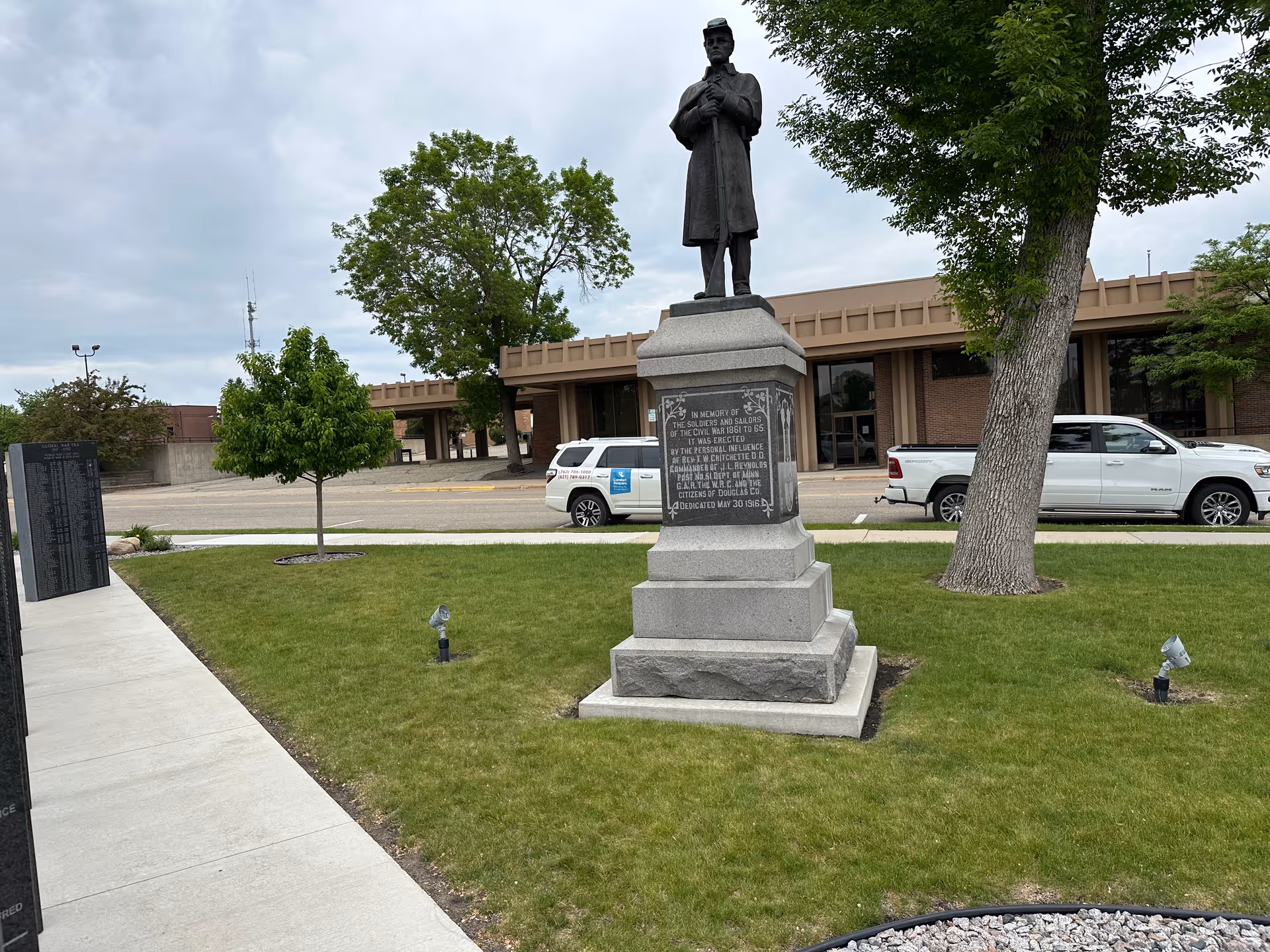 Statue on a pedestal in a grassy plaza with a brick building behind.