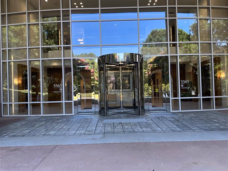 Glass-front entrance of a modern building with revolving doors and reflections.