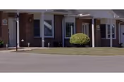 A single-story brick senior living facility with a covered entrance and manicured shrubs.